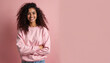© Viktor - Indian woman in pink sweatshirt smiles. Happy young female poses isolated on pastel pink background. Wears casual clothes. Joyful, confident girl with long curly hair looks to camera. Copy space for