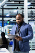 © DC Studio - African american business person walks through modern factory inspecting solar panel machinery, reading important insight for the corporate commitment to sustainability and renewable power.