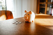 © Westend61 - Piggy bank and coins on a wooden table representing savings and financial planning indoors