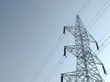 High voltage power lines on towering steel pylons transmit electrical energy across the blue sky