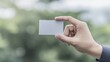 © ParinApril - Blank Business Card in Hand Against a Soft-Focused Green Background for Custom Branding Applications and Mockups