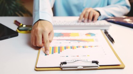 Poster - Business professional analyzing charts and graphs on documents while typing on keyboard at a modern workspace