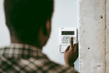 Man setting security system at home in the afternoon, focusing on keypad and monitoring device for safety