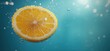 © Vergiliy - Fresh lemon slice submerged in sparkling water with bubbles and blue background