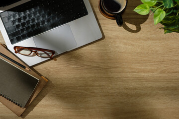 Wall Mural - Top view of modern wooden desk with laptop, notebook, coffee cup, and eyeglasses in natural lighting.