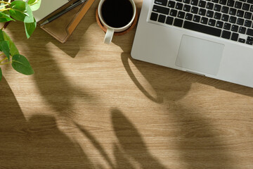 Wall Mural - Top view of wooden desk with laptop, notebook, coffee cup, and potted plant in natural lighting.