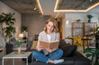 © Migma_Agency - Woman reading a book at home on the sofa in her living room