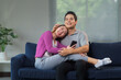 © Crystal - Happy asian couple is spending time together on the sofa at home, using a smartphone and smiling