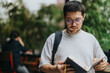 © qunica.com - A focused high school student with a backpack reads a book while standing in a park, surrounded by greenery. The student wears casual clothing and glasses, conveying a relaxed and studious atmosphere.