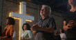 © Marco - Elderly man clapping during church worship, illuminated cross in background, diverse group expressing faith, unity, and devotion in religious indoor gathering