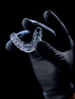 © Antony - Transparent dental aligners — modern braces for teeth straightening in cosmetic dentistry and orthodontics, held in the hand of a person wearing a black medical glove.