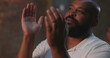© Marco - Man lifting hands and clapping in worship, African American man in white shirt with beaming expression during evangelical church service, spiritual joy and celebration