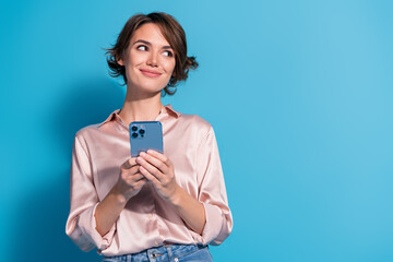 Poster - Young businesswoman wearing elegant satin shirt holding smartphone against blue background