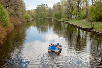 Fototapete - Two People Enjoying a Peaceful Boat Ride on a Serene Lake Surrounded by Lush Greenery in Springtime