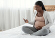 © Prostock-studio - Smiling Black Pregnant Woman Sitting With Smartphone On Bed At Home, Looking At Cellphone Screen With Excitement, Happy African Lady Browsing Pregnancy App Or Received Mobile Offer, Copy Space