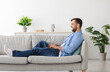 © Prostock-studio - Happy adult european man with beard sitting on sofa and typing on laptop in living room interior, profile, copy space. Guy plays in online game at free time, chat on social networks and work remotely