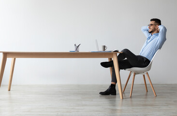 Aufkleber - Taking Break. Profile side view of smiling young Arab man relaxing on chair sitting at table and using laptop, happy millennial male leaning back at workplace, looking at pc screen watching video