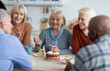 © Prostock-studio - Healthy and active positive senior people of different nationalities sitting at kitchen, drinking tea and eating cake together, having conversation and laughing, chilling together at nursing home
