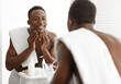 © Prostock-studio - Happy Black Man Touching Smooth Face Skin After Shaving Standing Near Mirror In Bathroom At Home. Male Facial Skincare, Morning Beauty Routine And Self-Care Cosmetics Concept