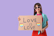 © Pixel-Shot - Beautiful young woman holding placard with text LOVE IS LOVE on lilac background. LGBT concept