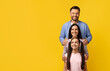© Prostock-studio - Happy Young Family, Mother Father And Daughter Embracing While Standing In Line, Cheerful Caucasian Parents And Teen Female Child Bonding Together, Posing On Yellow Studio Background, Copy Space