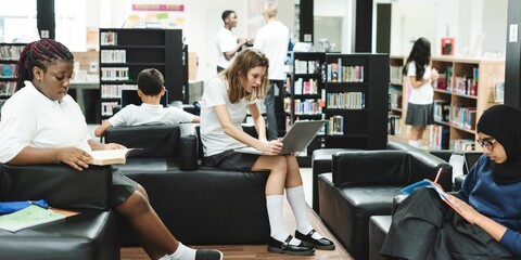 Poster - Students in a library, reading and using laptops. Diverse group, including young women and men, engaged in study. Library setting with books and technology. Female student reading in library.
