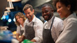 © Curioso.Photography - Smiling team of chefs and kitchen staff working together in a professional restaurant kitchen.