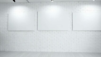 Poster - White brick wall backdrop with three blank canvases and track lighting, an exhibition setting
