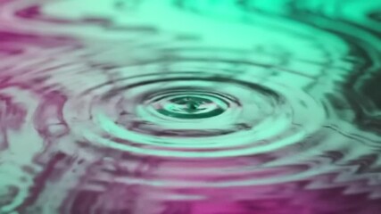 Poster - Slow motion shot of a water droplet creating ripples in a colorful liquid surface