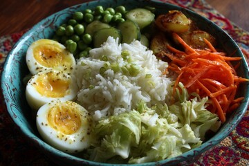 Poster - Colorful bowl of rice with boiled eggs, vegetables, and spices served in a traditional dish at a rustic kitchen setting