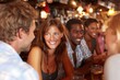 © whitestorm - Group of diverse young adults enjoying drinks and conversation at a lively bar, laughing and socializing over beverages after work during happy hour.