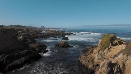 Wall Mural - Tranquil coastal scene featuring gentle waves crashing rocky shore under blue sunny sky