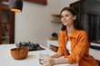 © SHOTPRIME STUDIO - Young woman in an orange shirt enjoying a refreshing drink in a modern kitchen, embodying a healthy lifestyle and positive emotions