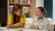 © Yuliia - Caucasian little funny kids children friends talking in school classroom studying together laughing girls tell secret whisper gossip have fun conversation schoolgirls pupils students education indoors