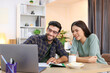 © unikyluckk - Business couple working, communicating while sitting at the home office desk together. Cheerful couple, calm asian woman and caucasian man working at home with laptop together.