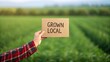 © ANNetz_PK - Fresh Organic Food at Local Farmstand Market Series, A hand in a flannel sleeve holds up a locally grown vegetable against a neutral background.