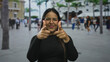 © Krakenimages.com - Smiling woman points fingers with confidence on a bustling street with people strolling by during a sunny day.
