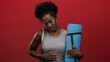 © Krakenimages.com - Woman holds stomach and yoga mat over isolated red background, expressing discomfort.