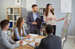 © Studio Romantic - Young woman talking about company growth and finance discussing job project on meeting. Business people employees sitting in modern office with colleagues on work conference. Teamwork concept