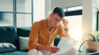 © FlexiTon/peopleimages.com - Stress, man and reading document at house financial crisis, payment notice and debt pressure. Frustrated, male person and paperwork for bank repossession, loan rejection and eviction letter in lounge