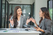 © panomporn - Two professional businesswomen are working on laptop computers sitting at desks in the office. Colleagues are happy and discussing the digital strategy of the Graph