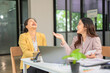 © panomporn - Two professional businesswomen are working on laptop computers sitting at desks in the office. Colleagues are happy and discussing the digital strategy of the Graph