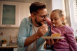 © Drazen - Happy father and daughter eating sweet pie in kitchen.
