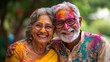 © liliyabatyrova - Elderly Indian couple joyfully celebrating Holi festival with vibrant colors and laughter in their home garden