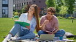© stockbusters - Focused couple working project together on green campus lawn. Young students