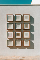 Poster - A collection of square frames hanging on a white wall under a clear blue sky in the bright sunlight