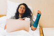 © Juanmarcos - Woman with broken arm using laptop and smartphone in bed