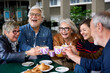 © CarlosBarquero - Group laughing mature people having snack sitting at cafe bar. Older friends toasting with coffee cups gathered together in terrace restaurant. Food and beverage lifestyle in senior citizens concept