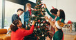 © Wesley25/peopleimages.com - Christmas, decoration and tree with friends in living room of home for celebration or social event. December, ornament and party with group of happy people in apartment together for holiday season