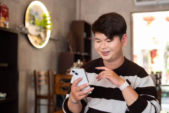 young happy gay man in cafe texting with mobile phone